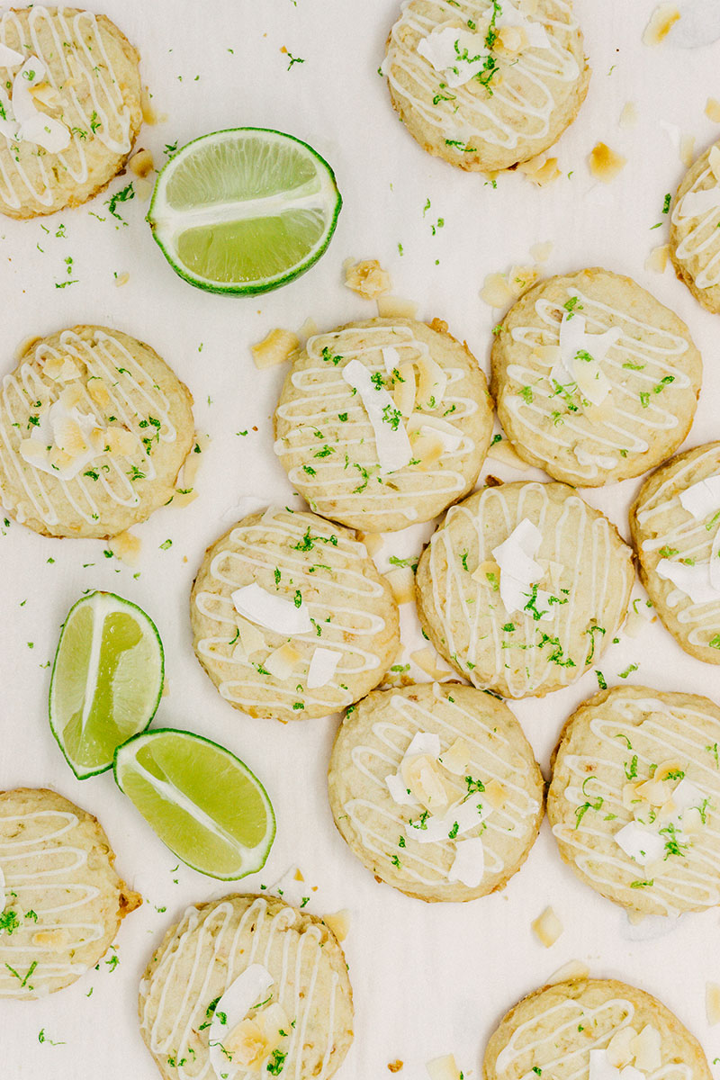 taste before beauty coconut lime shortbread cookies scattered on a table with limes and coconut flakes surrounding