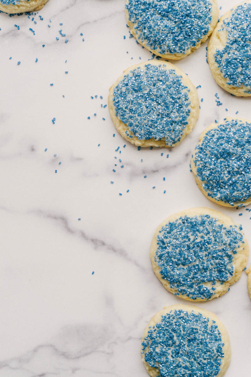 taste before beauty buttery sugar cookies spread out on a marble slab with blue sprinkles