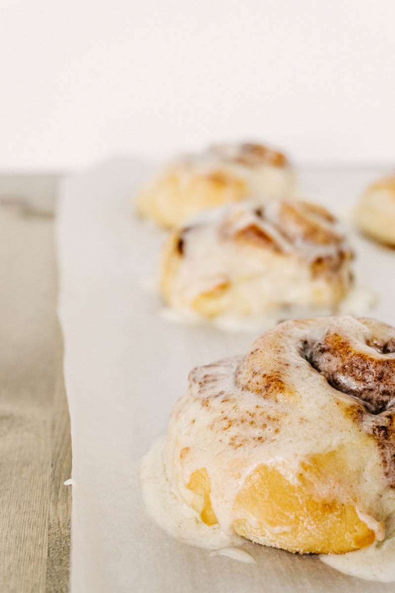 cinnamon rolls on parchment paper with cream cheese frosting melted over the top