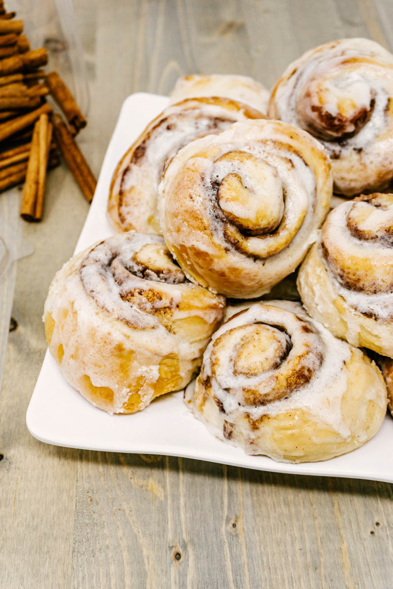 cinnamon rolls with cream cheese frosting on a plate with cinnamon sticks