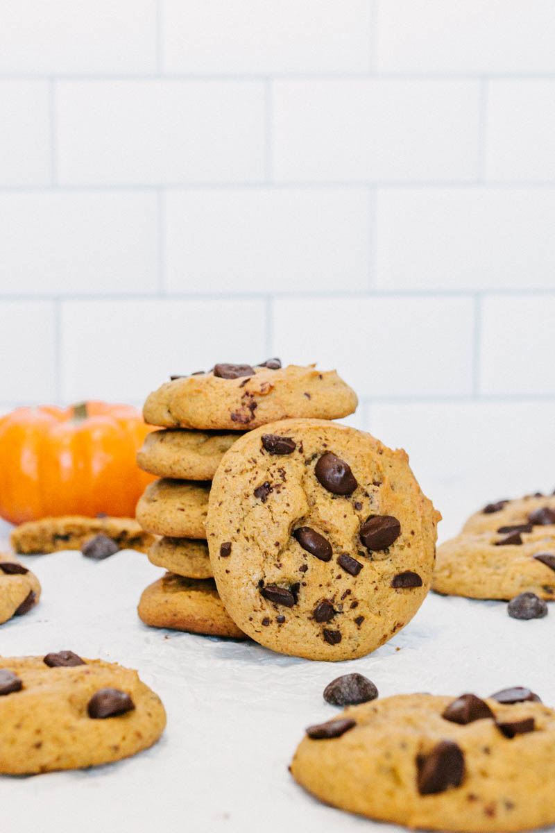 taste before beauty pumpkin chocolate chip cookies on parchment paper with chocolate chips and pumpkins stacked on top of each other