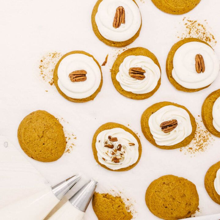 pumpkin cookies being frosted with cream cheese frosting