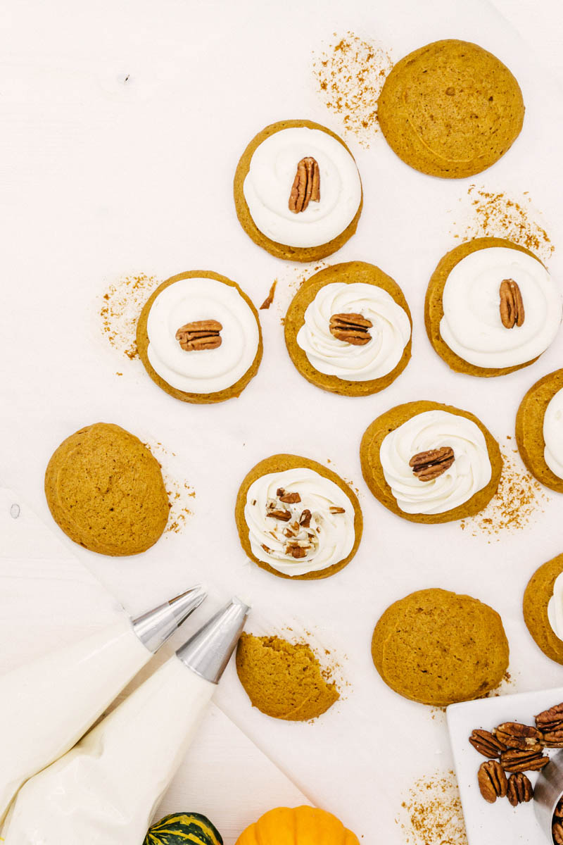 pumpkin cookies being frosted with cream cheese frosting