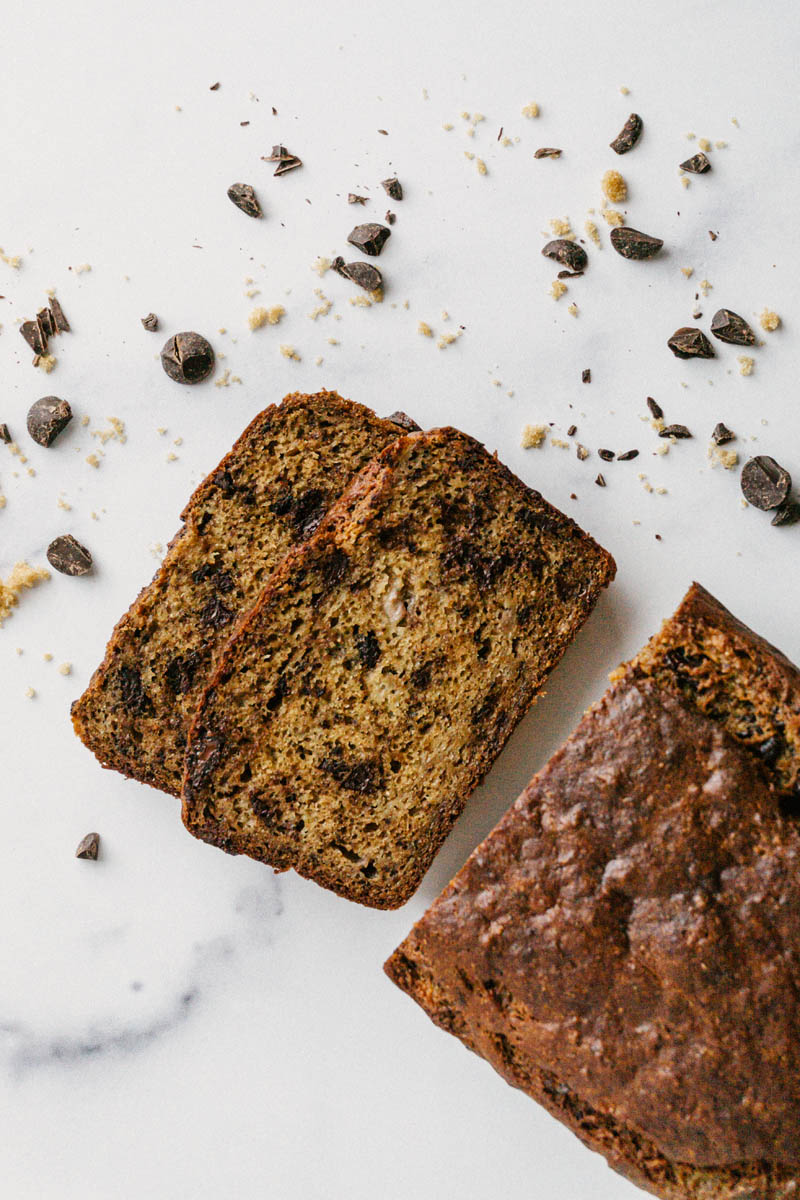 taste before beauty healthy chocolate chip banana bread and slices on marble top with chocolate chips around