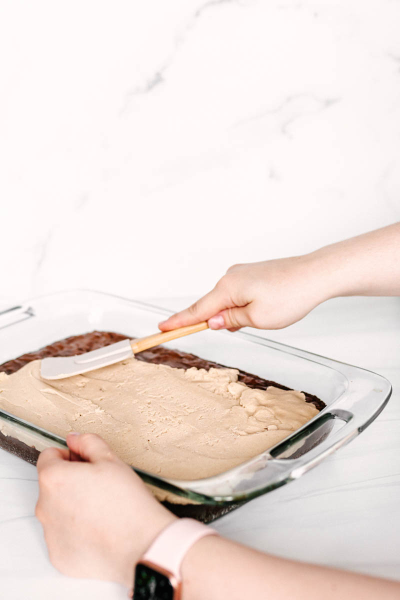 spreading cookie dough topping on brownie base