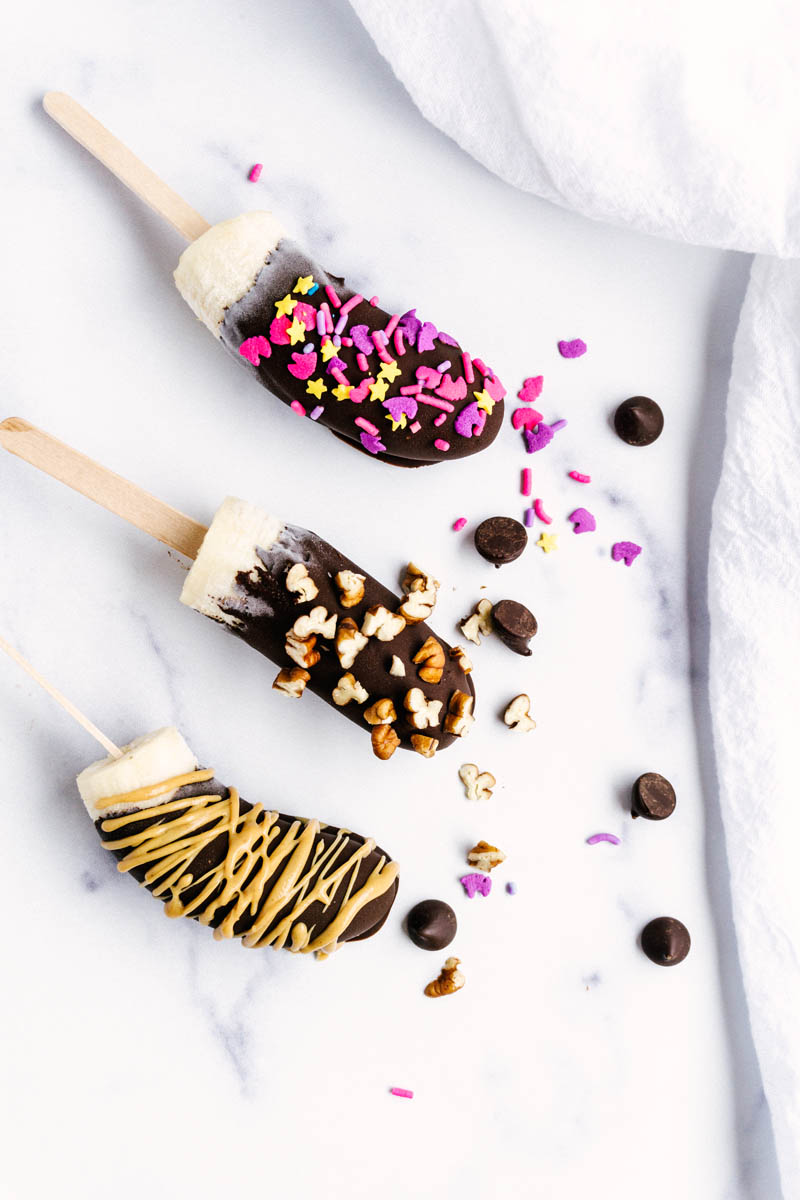 frozen chocolate covered bananas with toppings on the table