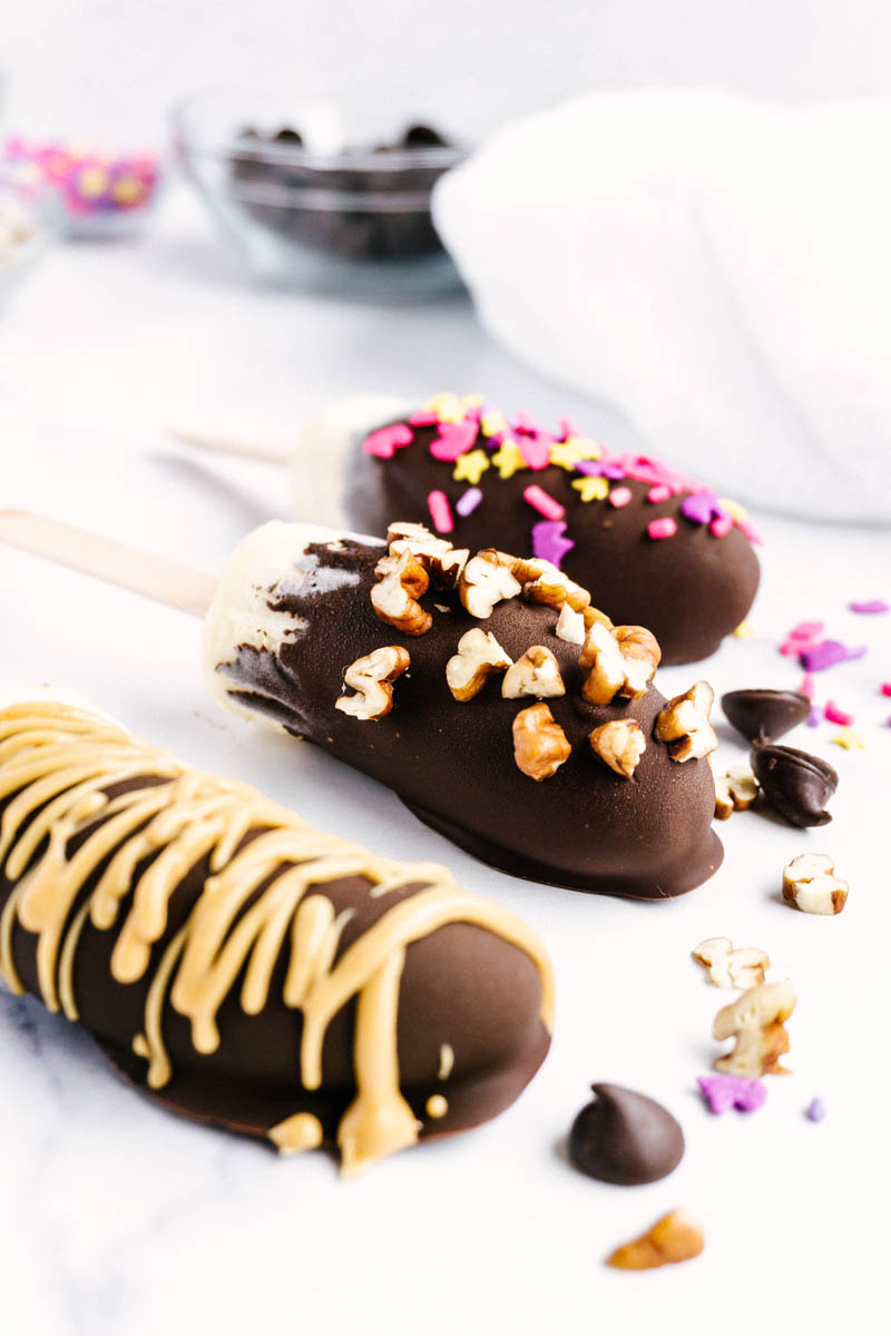 frozen chocolate covered bananas on the table with toppings spread out