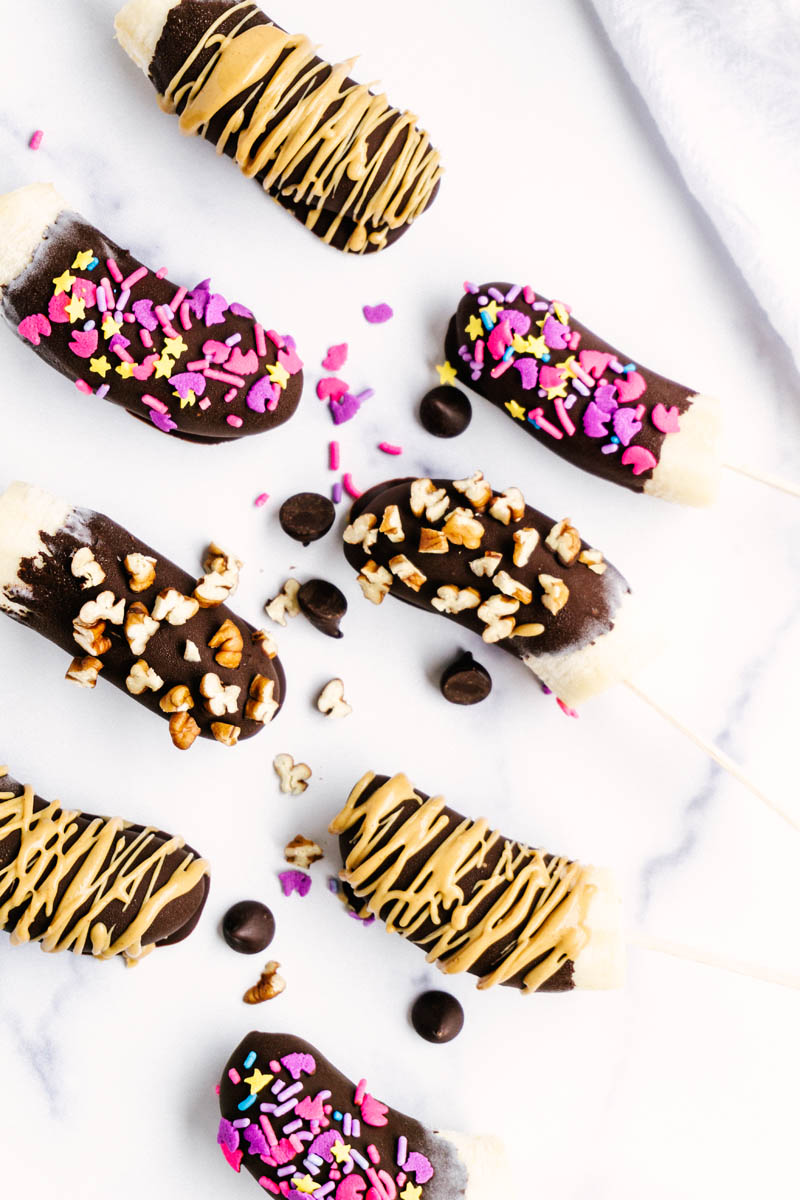 frozen chocolate covered bananas layed on the taable with sprinkles surrounding
