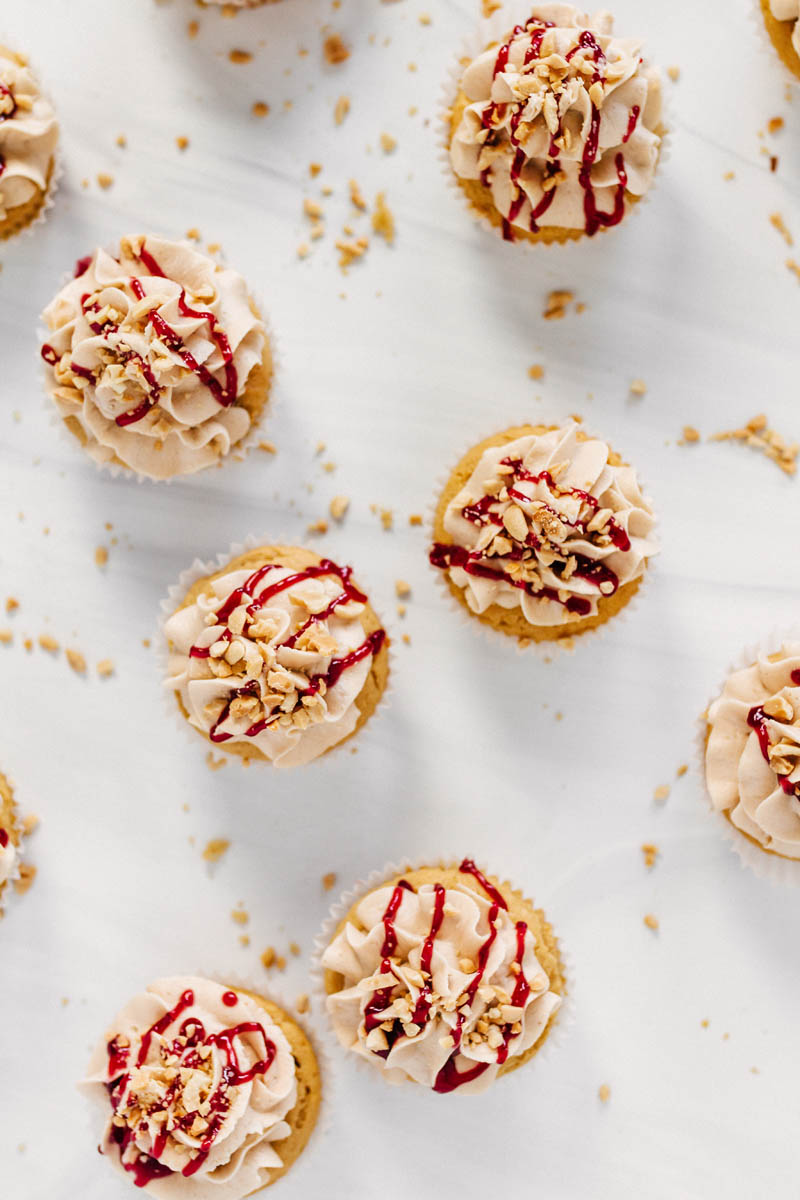 peanut butter and jelly cupcakes on table with peanuts and jam drizzle