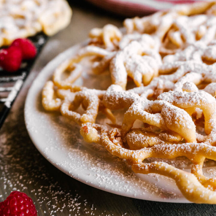 funnel cake with powdered sugar on platae with raspberries