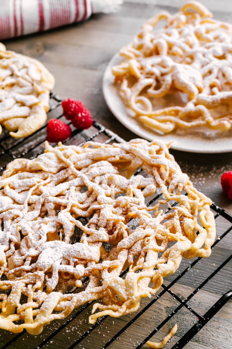 funnel cakes on plates and cooling wire racks with raspberries and powdered sugar