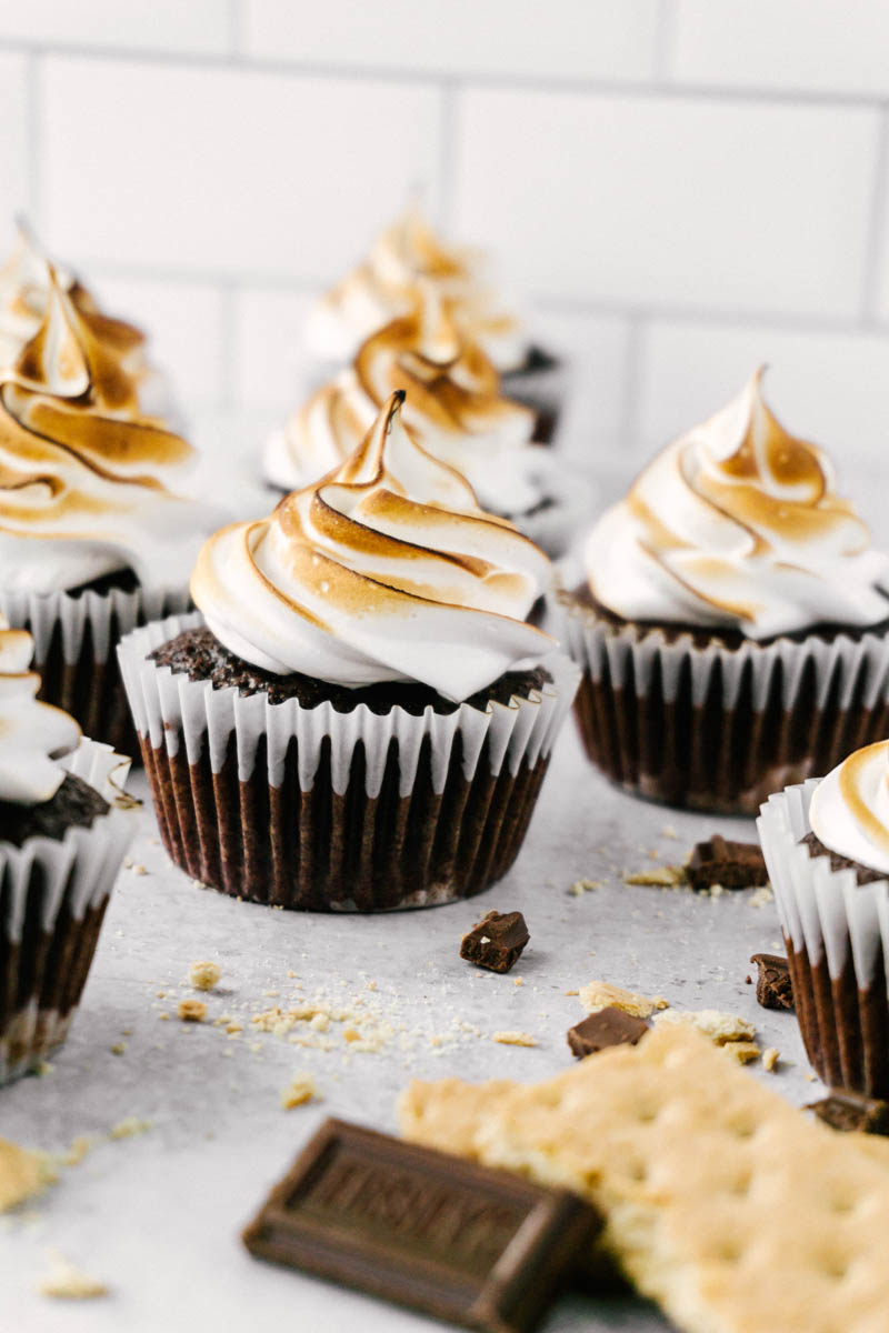 s'mores cupcakes on the table with chocolate and graham cracker pieces spread around