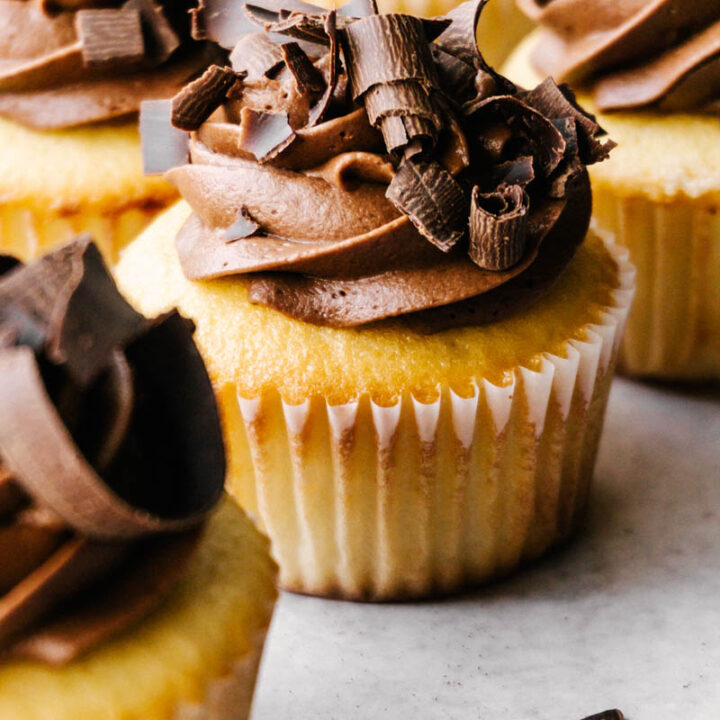 yellow cupcakes with chocolate buttercream frosting in liners on table