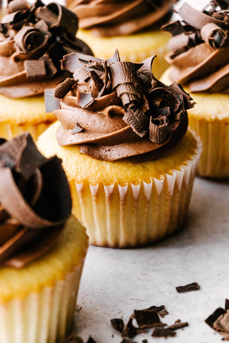 yellow cupcakes with chocolate buttercream frosting in liners on table