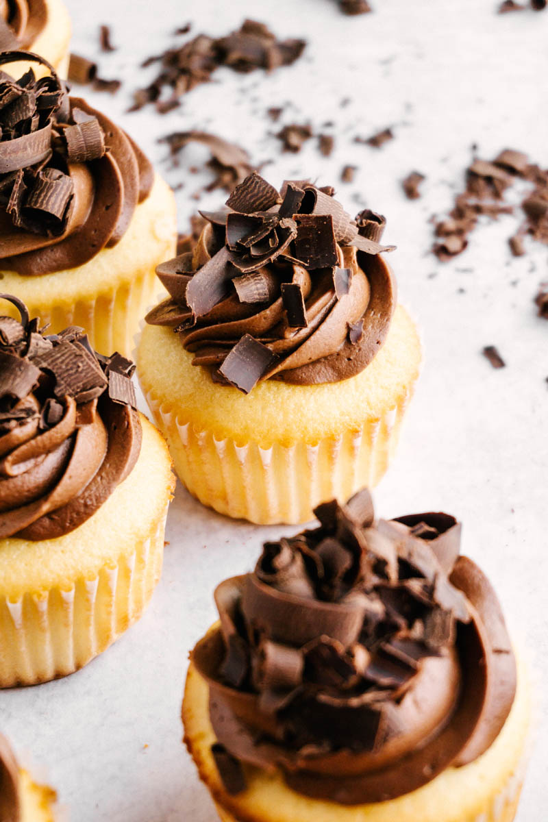 several yellow cupcakes with chocolate buttercream frosting on table with chocolate shavings