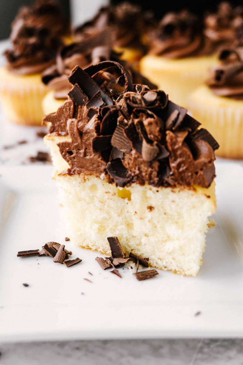 upclose yellow cupcakes with chocolate buttercream frosting cut in half on a plate