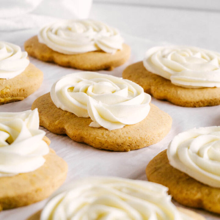 frosted pumpkin sugar cookies spread on parchment paper