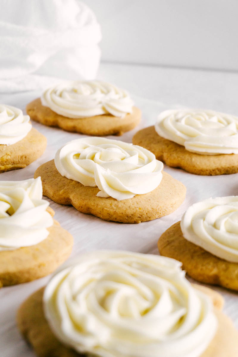 frosted pumpkin sugar cookies spread on parchment paper