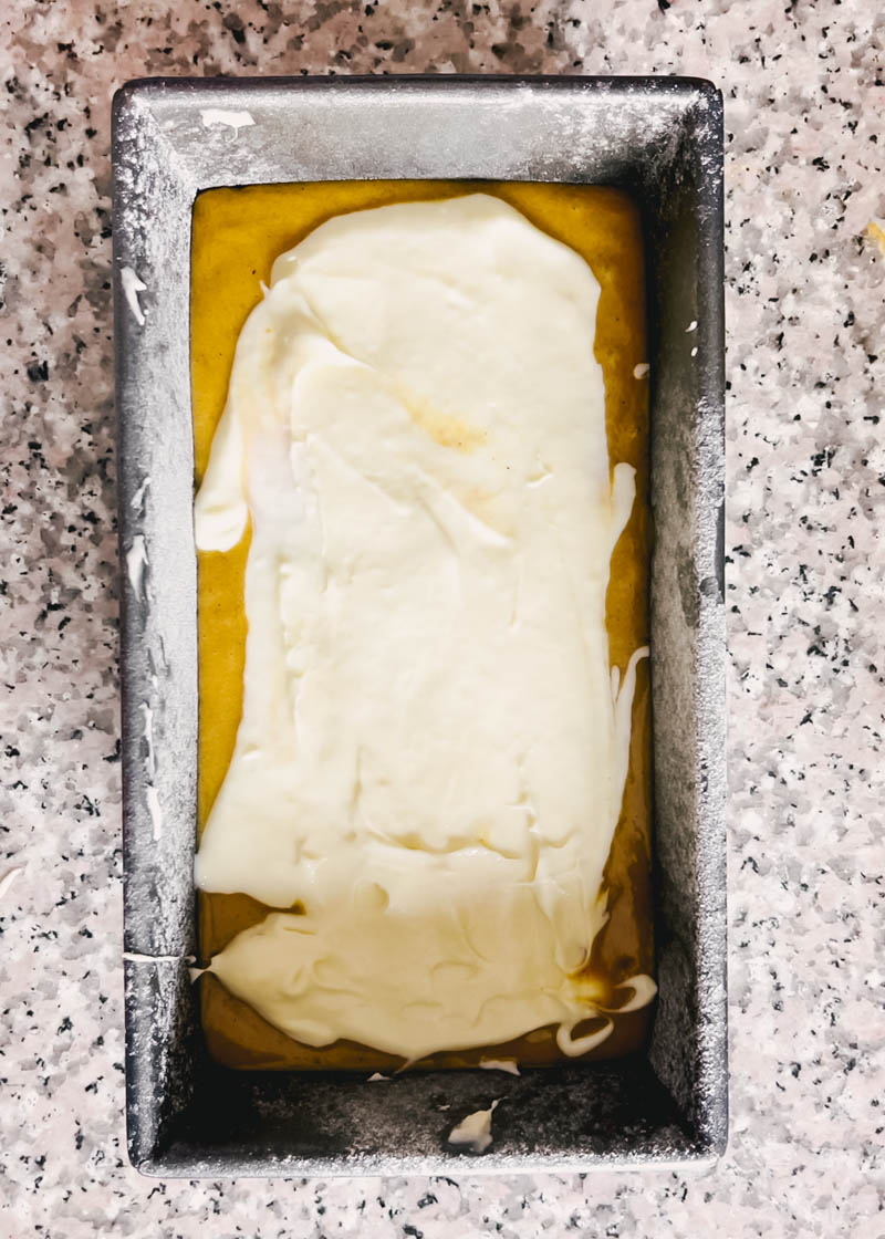 pumpkin bread batter in a loaf pan with cream cheese mixture on top