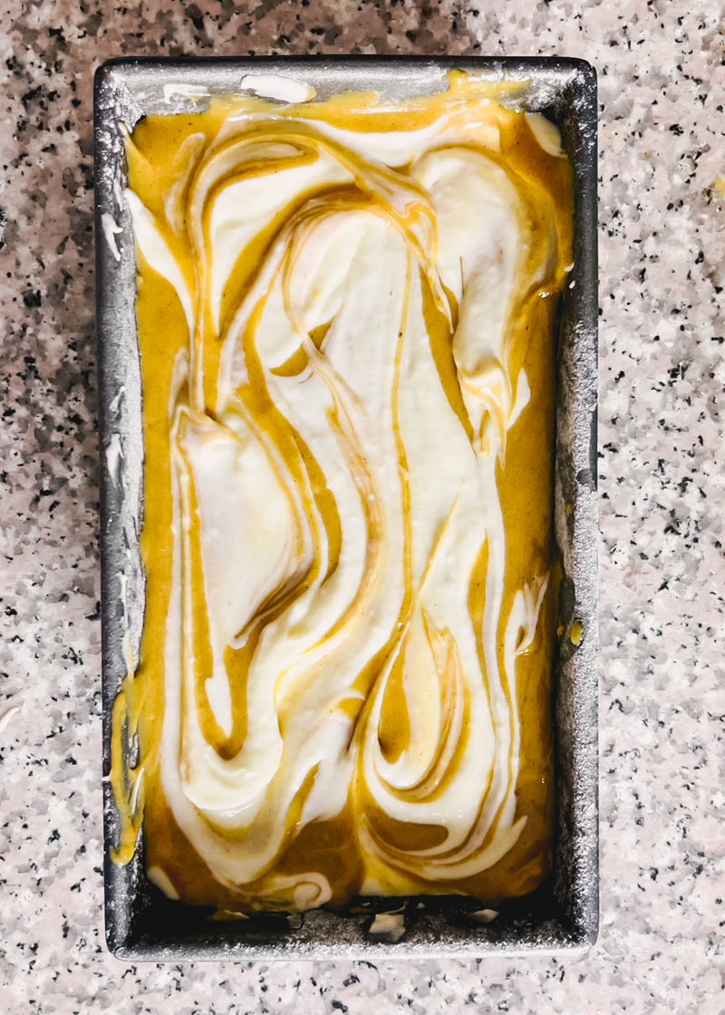 pumpkin bread batter in a loaf pan swirled with the cream cheese mixture