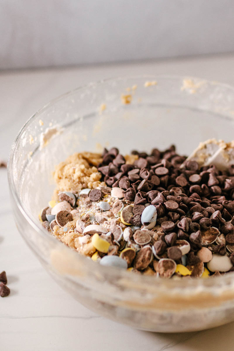 cookie dough in a mixing bowl with the unimxed chocolates on top