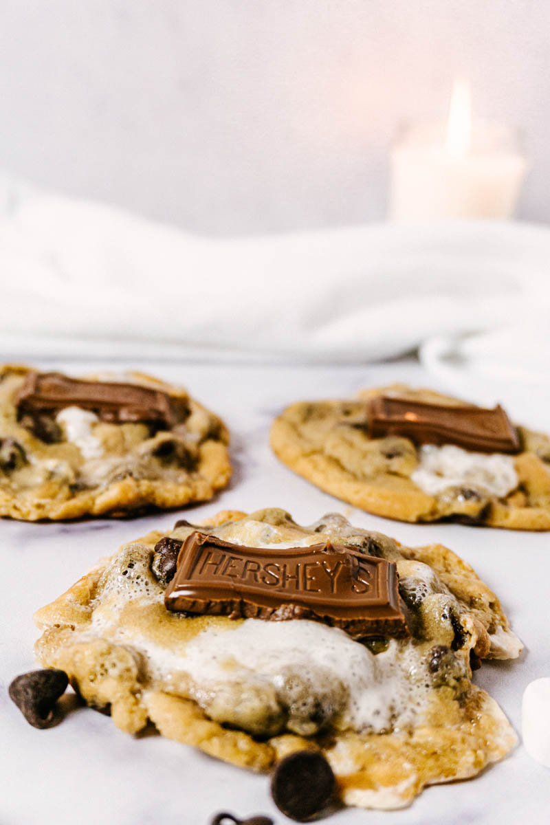 three s'mores cookies on a table with a candle in the back